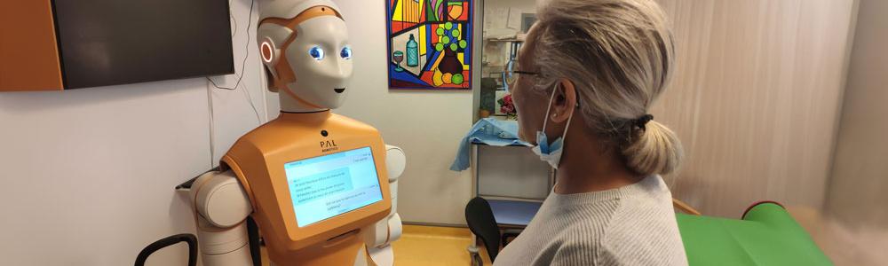 An orange robot called Ari speaks to a white woman.