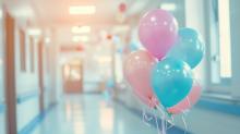A hospital corridor with a collection of balloons at the forefront of the image. They are pink, blue and purple.
