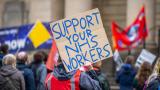 A group of people striking holding signs saying 'Support your NHS workers.'