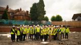 A group of people with hard hats and reflective jackets, standing on a building site.