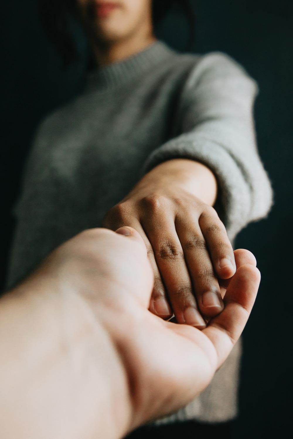 A child and an adult hold hands. the photo is taken from the adult's perspective, and is a close up of their hands touching.