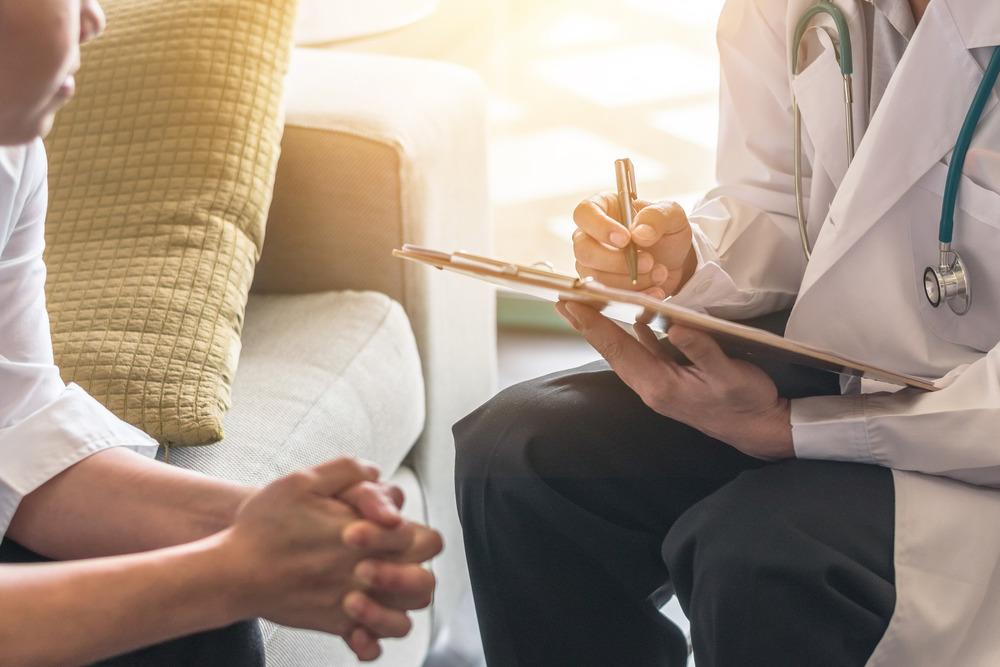 Two people sit opposite each other. One of them is holding a clipboard and writing some notes.
