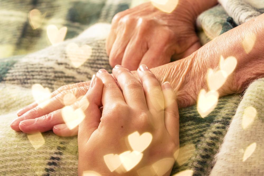 A young person holding an older person's hand on a tartan blanket.