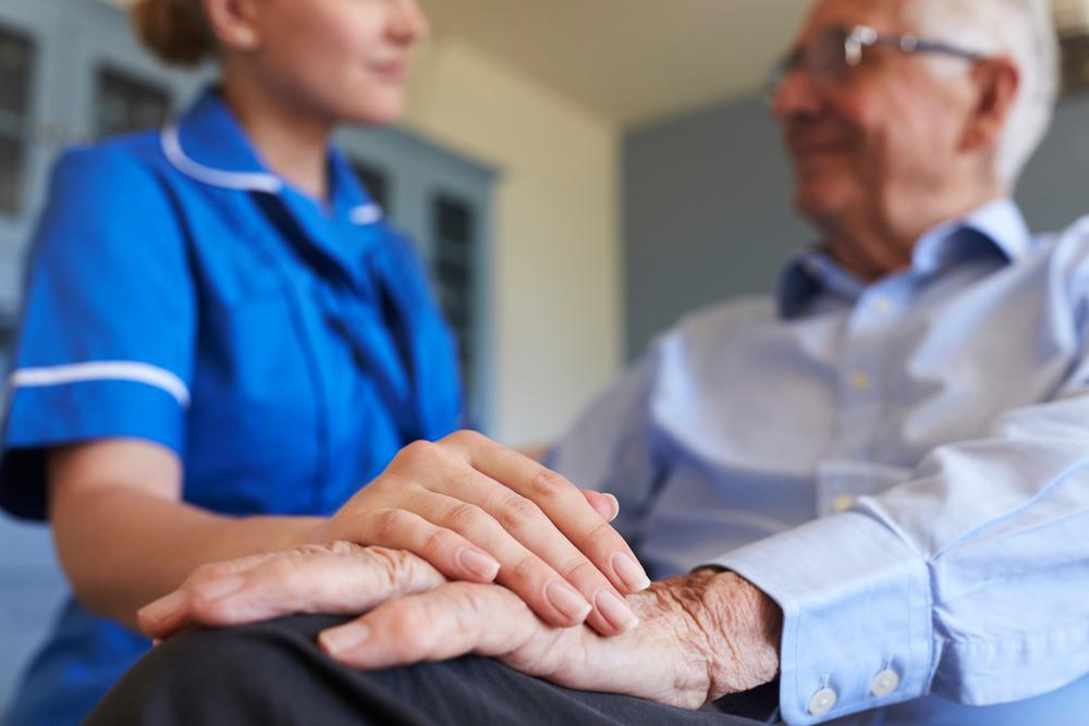 A nurse rests her hand on a patient's old hand.
