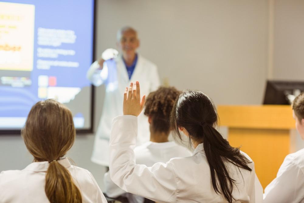 A class of medical students. One of them is raising their hands to answer a question from the lecturer.
