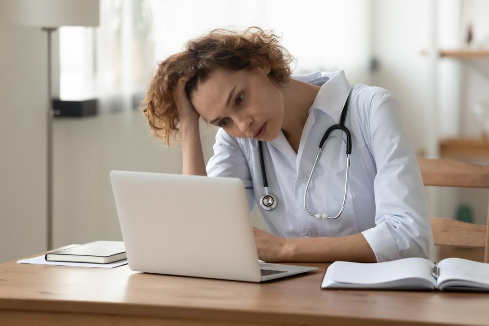 A doctor looking concerned and going on her laptop.