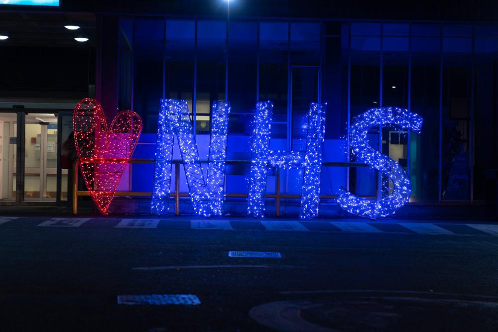 NHS in bright blue lights in the evening.