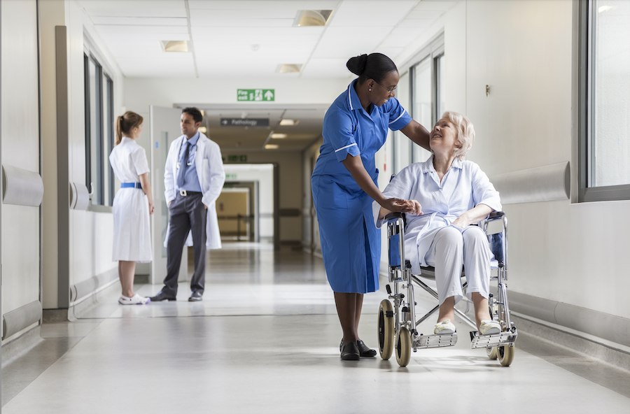A hospital corridor with 3 members of staff and a patient.