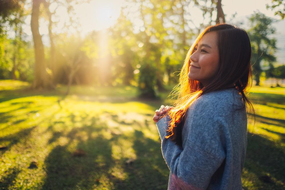 Person enjoying green space outdoors, surrounded by trees and sunlight.