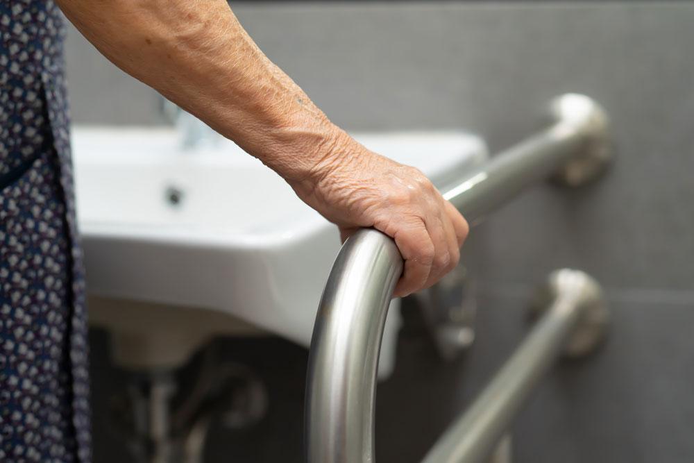 Elderly woman using handrail in bathroom
